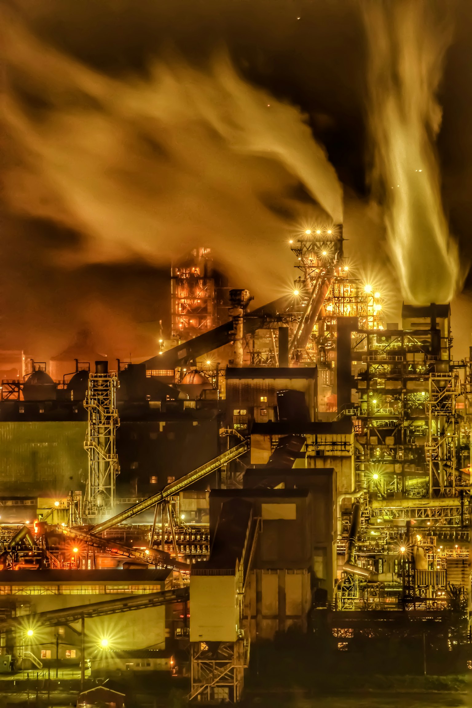 Night view of an industrial area with smoke and steam rising large smokestacks and factory equipment