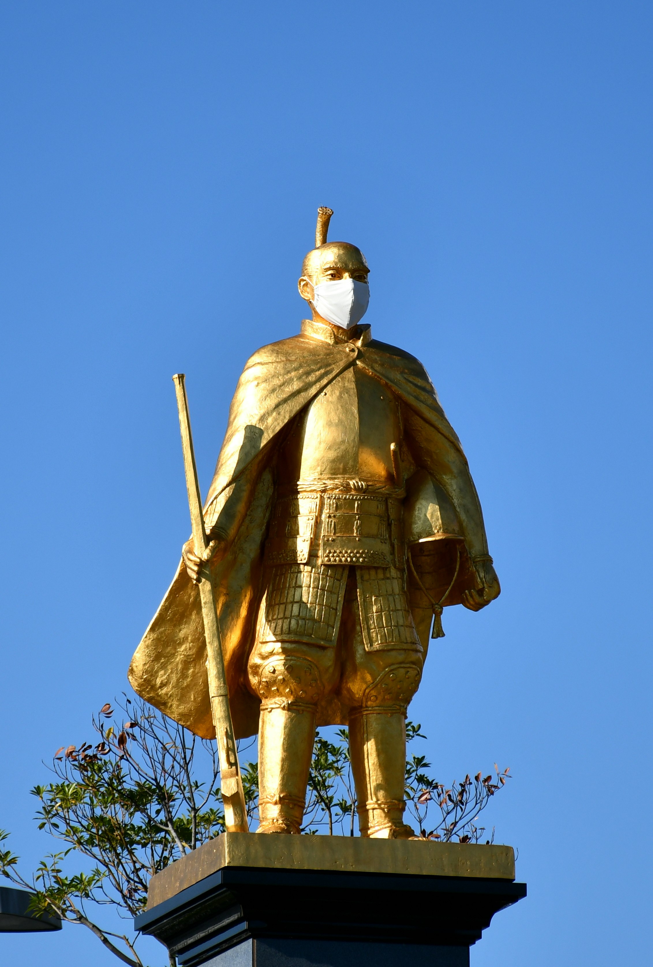 青空の下に立つ武将の金色の銅像