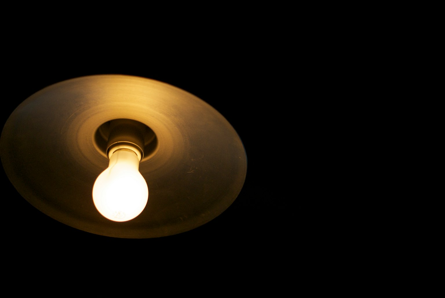 A hanging incandescent light bulb with a simple shade