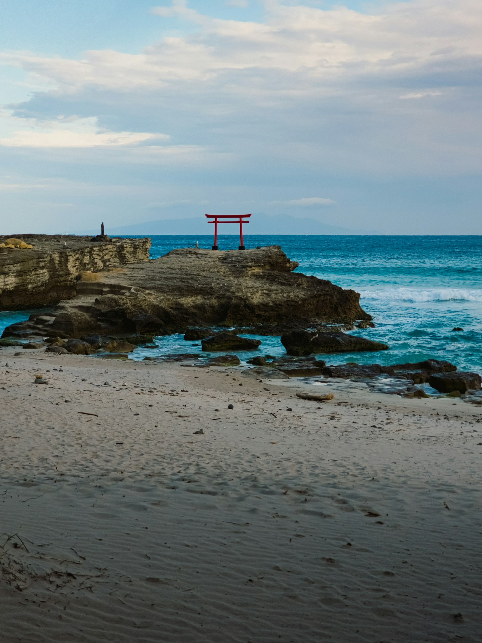 Vista escénica de un torii en una playa rocosa con olas del océano