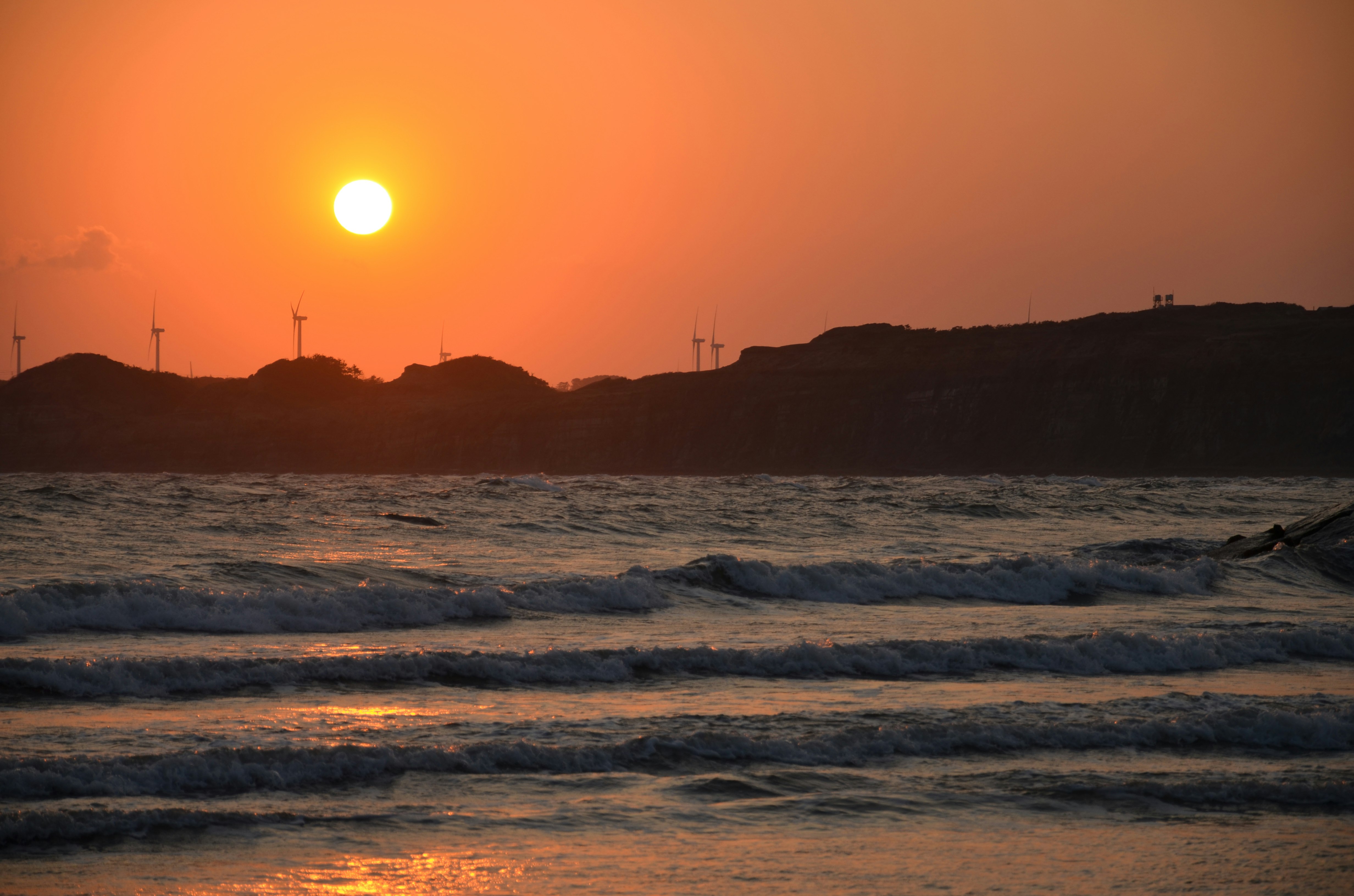 atardecer en una playa ventosa con olas y aerogeneradores