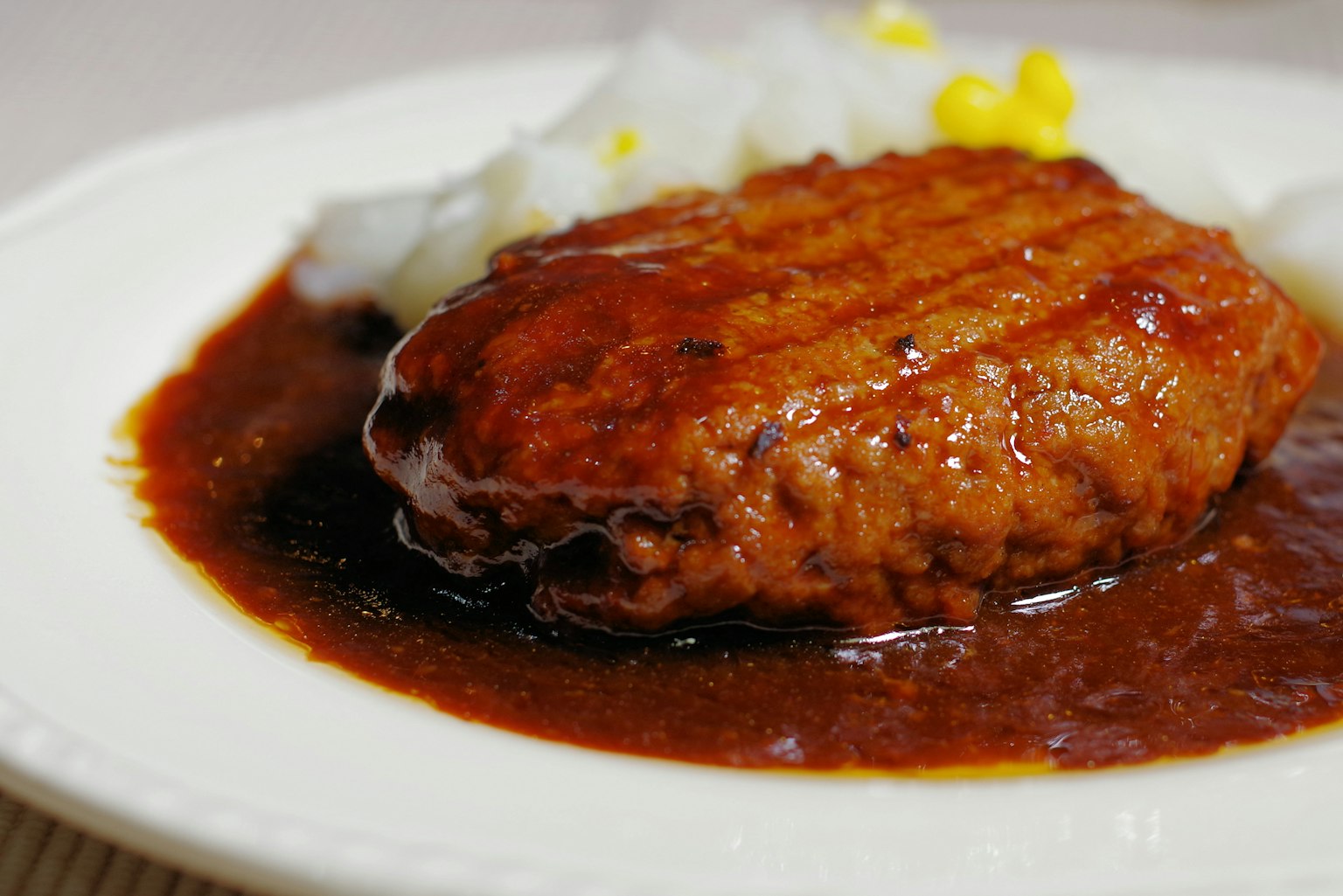 A hamburger steak served on a white plate with sauce