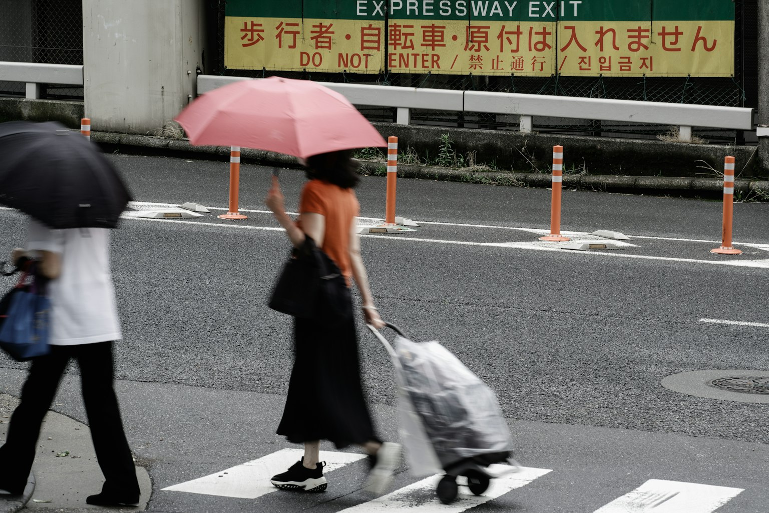一位拿着粉色雨伞的女性正在过马路，推着购物车