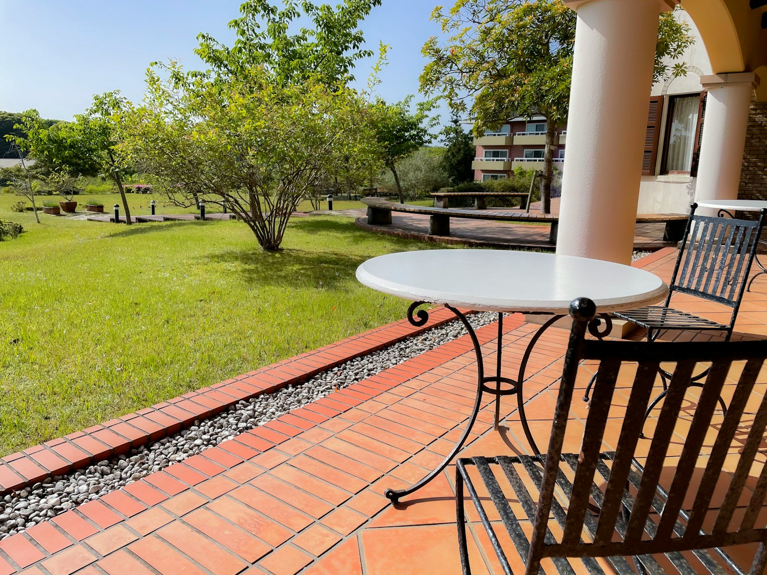 Ein weißer Tisch und ein Schmiedeeisenstuhl auf einer Terrasse mit Blick auf einen schönen Garten