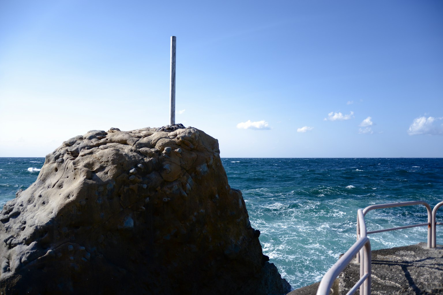 Costa rocosa con un poste bajo un cielo azul claro