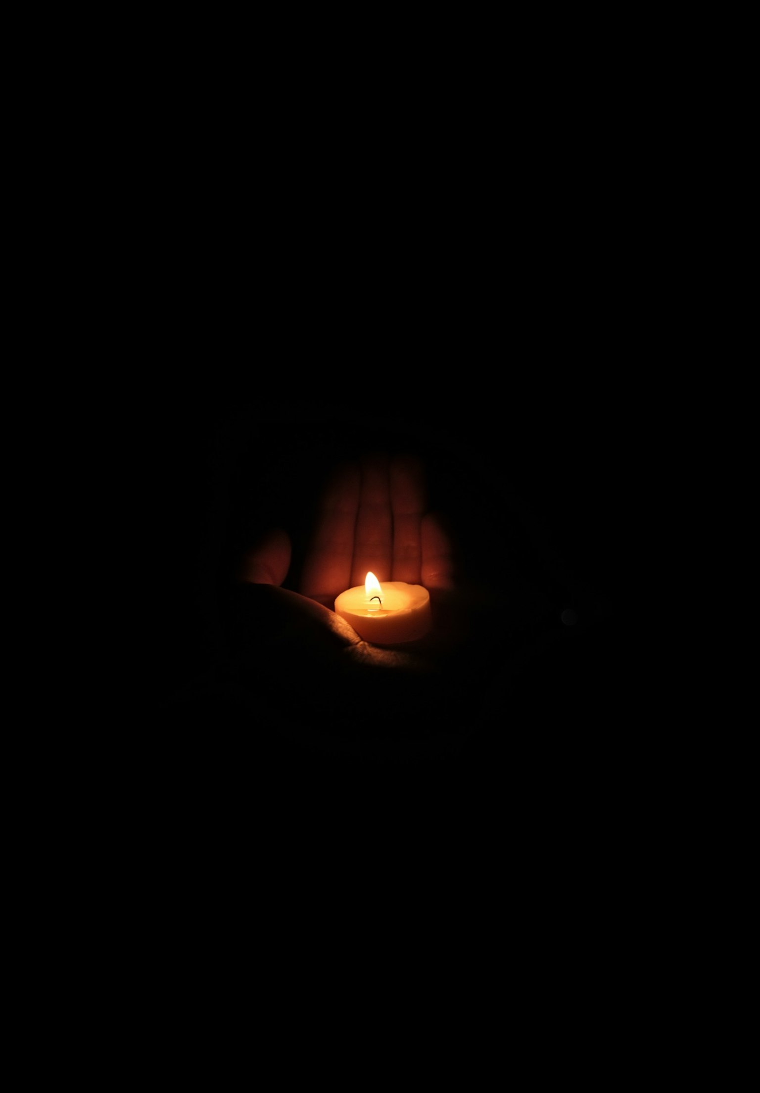 Eine kleine Kerzenflamme, die von Händen vor einem dunklen Hintergrund gehalten wird