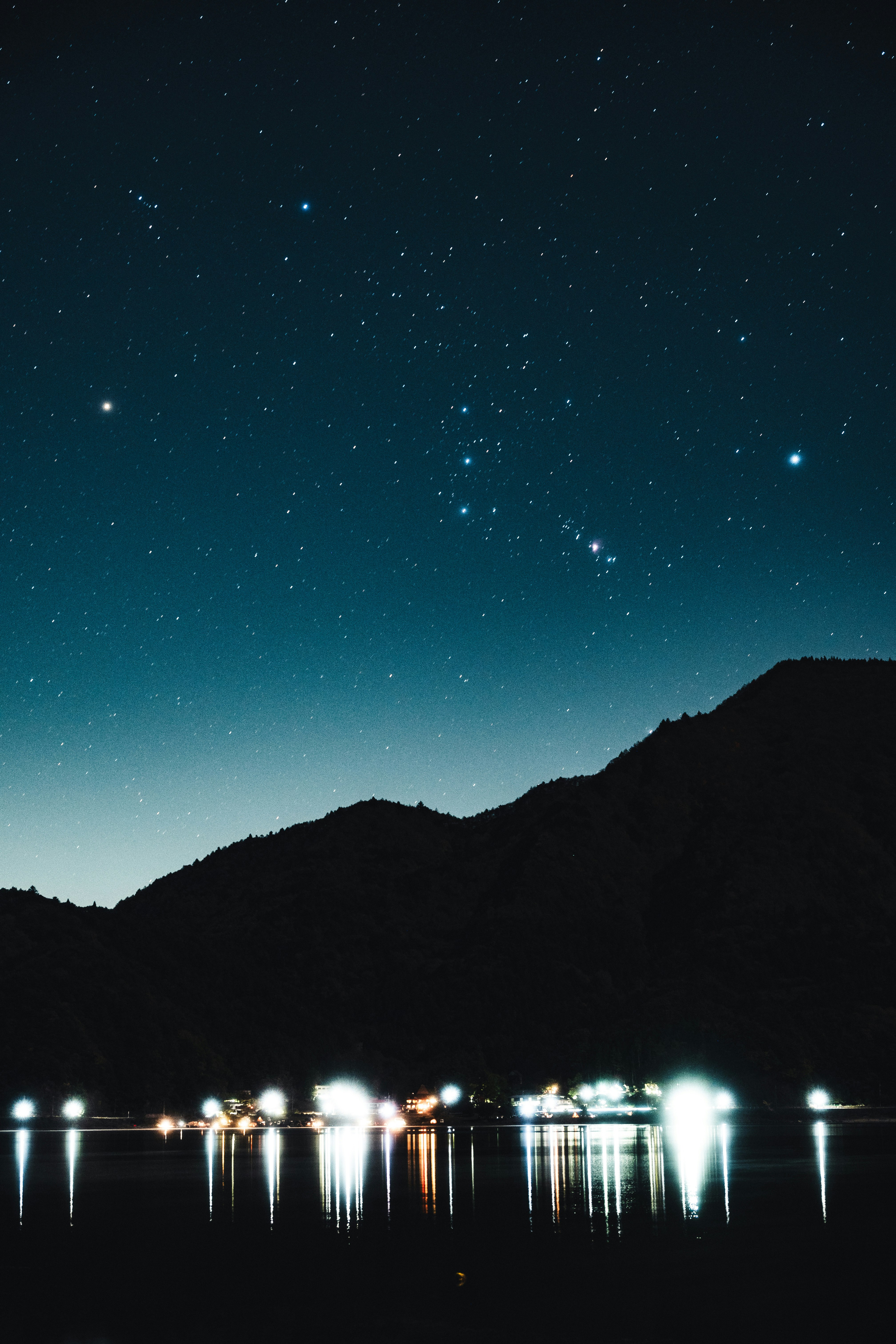 星空の下、湖面に映る灯りと山のシルエット