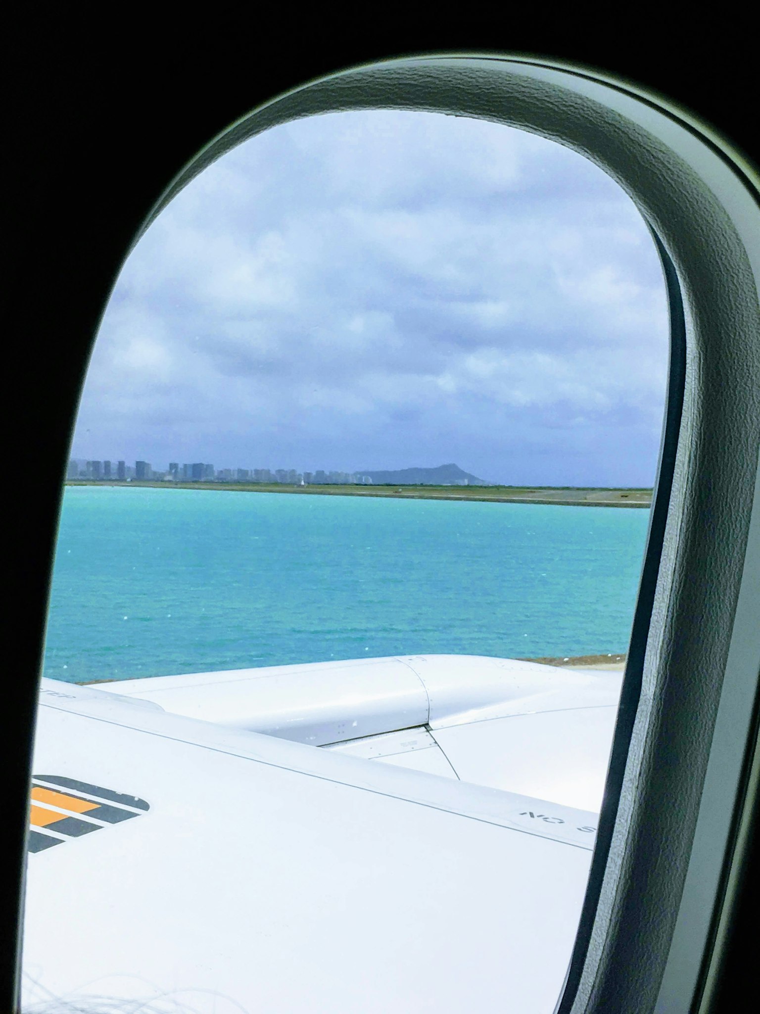 Blick auf das türkisfarbene Meer und den bewölkten Himmel aus einem Flugzeugfenster
