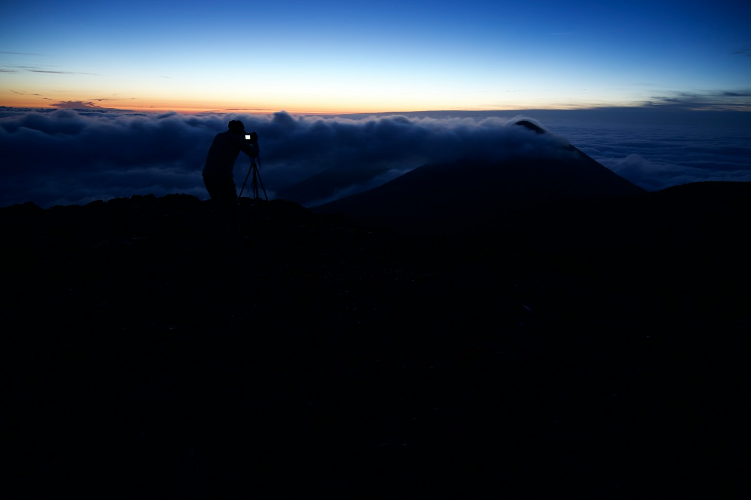 Personne avec un appareil photo au sommet d'une montagne au lever du soleil