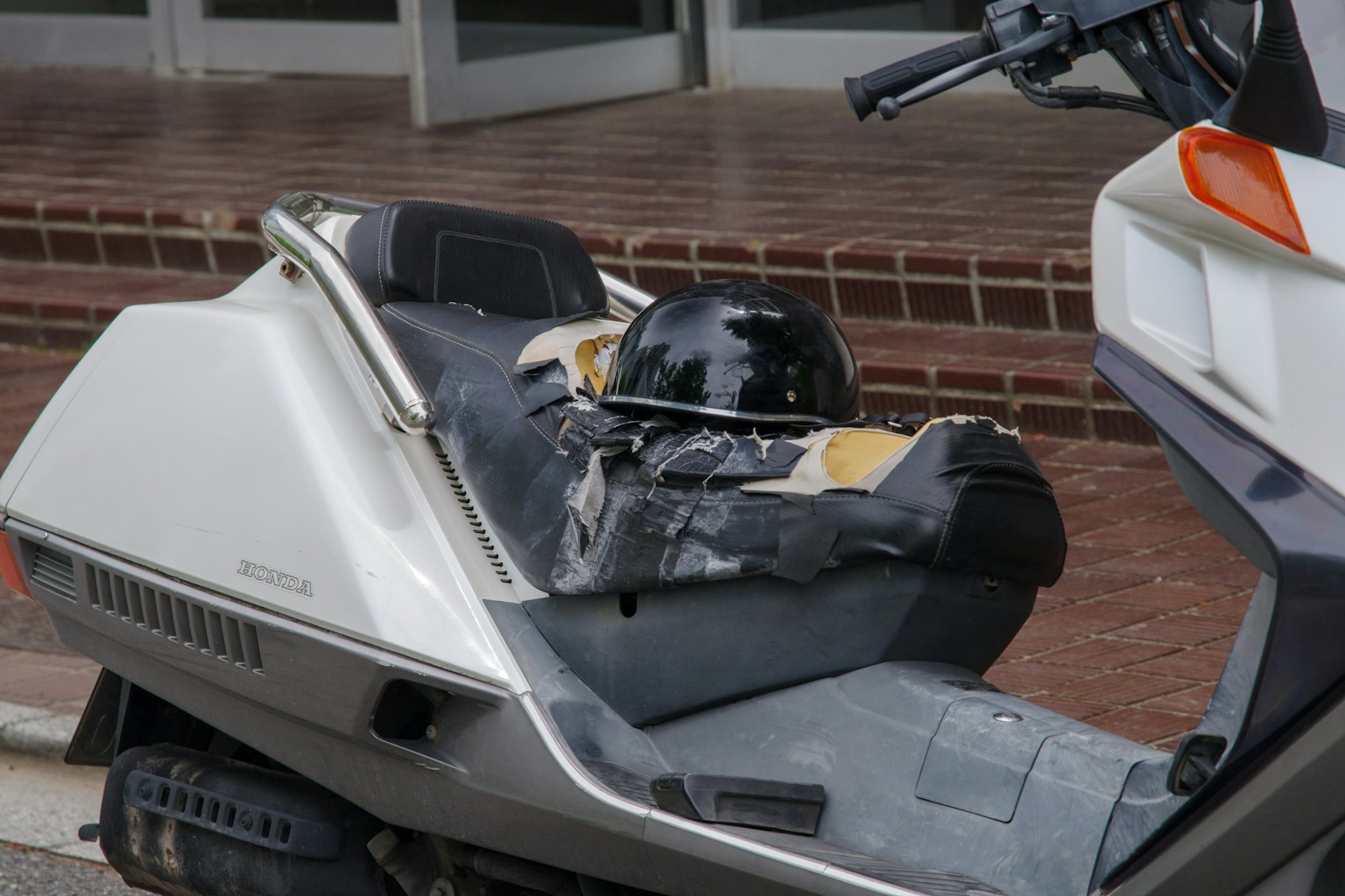 白いスクーターの座席に置かれた黒いヘルメットと擦り傷のある座面