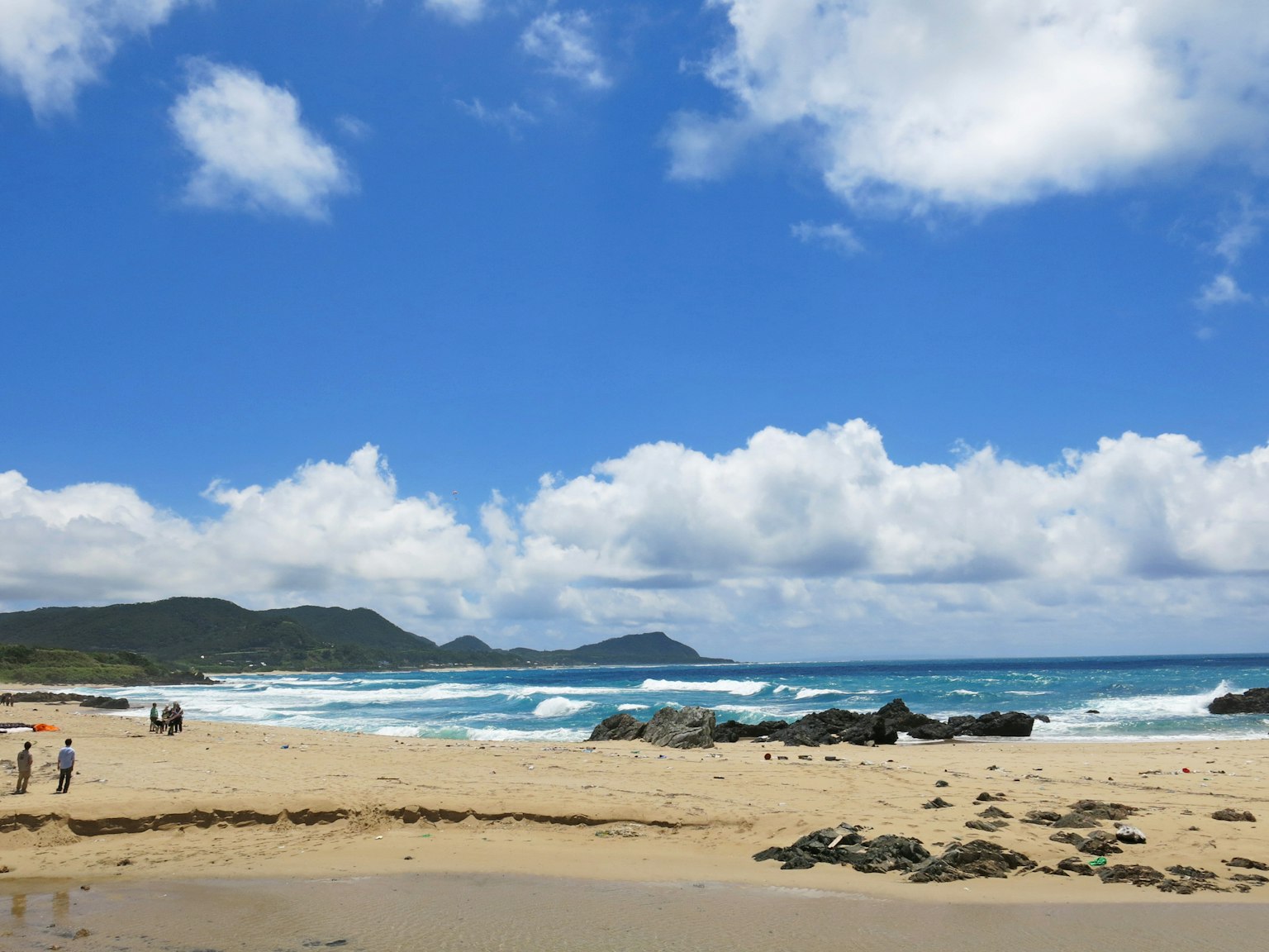 Beach scene with blue sky and white clouds featuring people walking