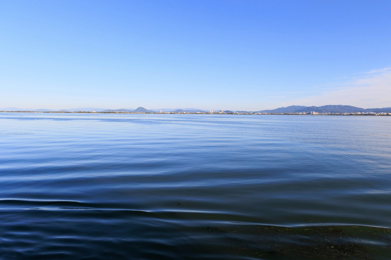 Paisaje de mar tranquilo y cielo azul Superficie de agua ondulada Montañas visibles a lo lejos
