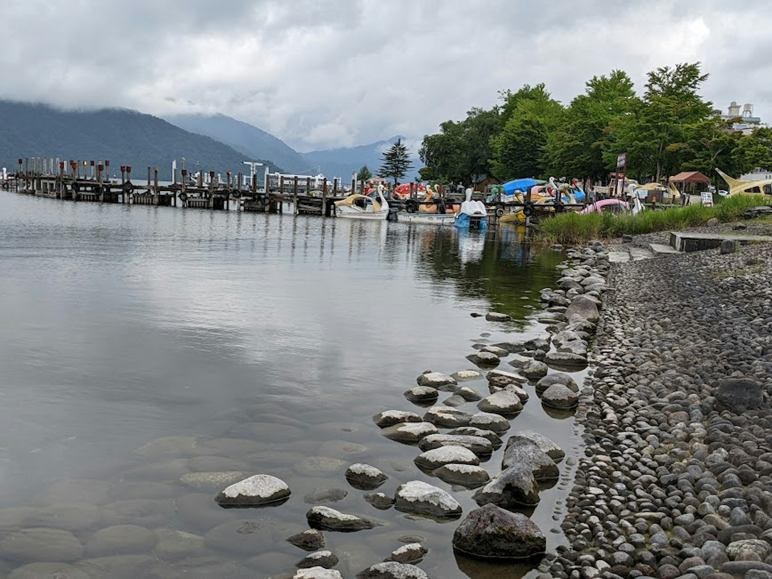 Ruhige Seeszene mit festgemachten Booten umgeben von grünen Bäumen und einem steinigen Ufer