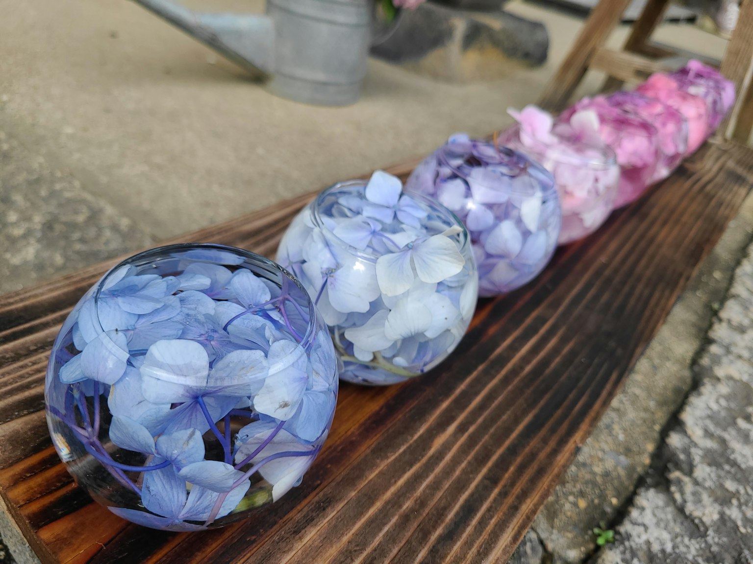 Dekorative Kugeln mit Hortensienblüten in Blau- und Rosatönen auf einer Holzoberfläche angeordnet