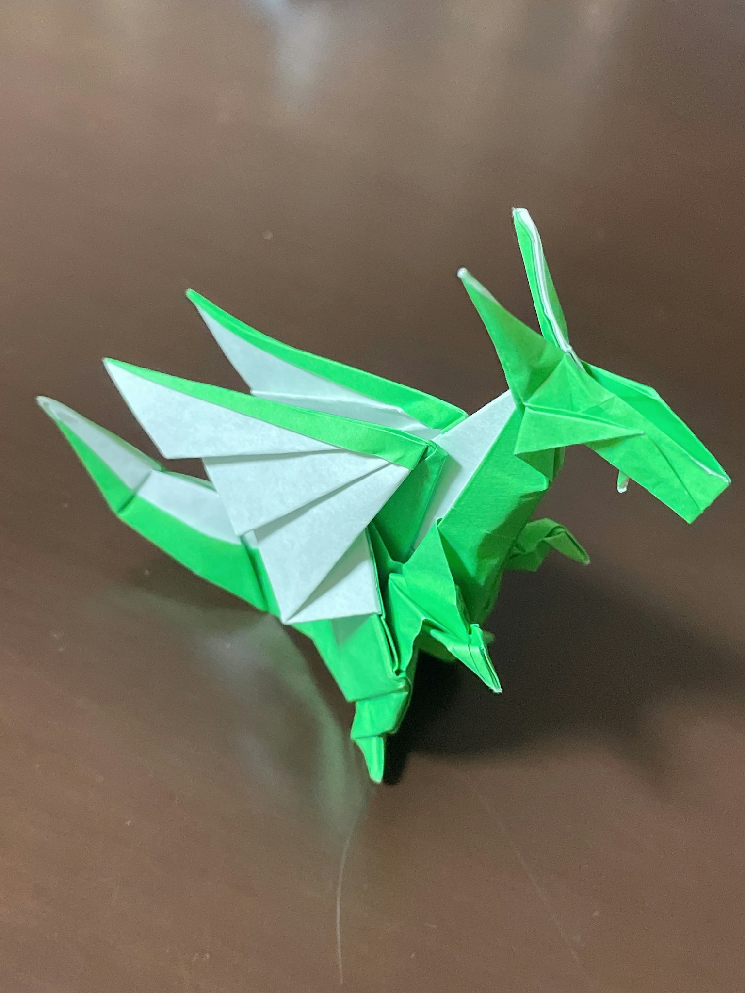 Grüner Origami-Drache mit weißen Flügeln, der aufrecht steht