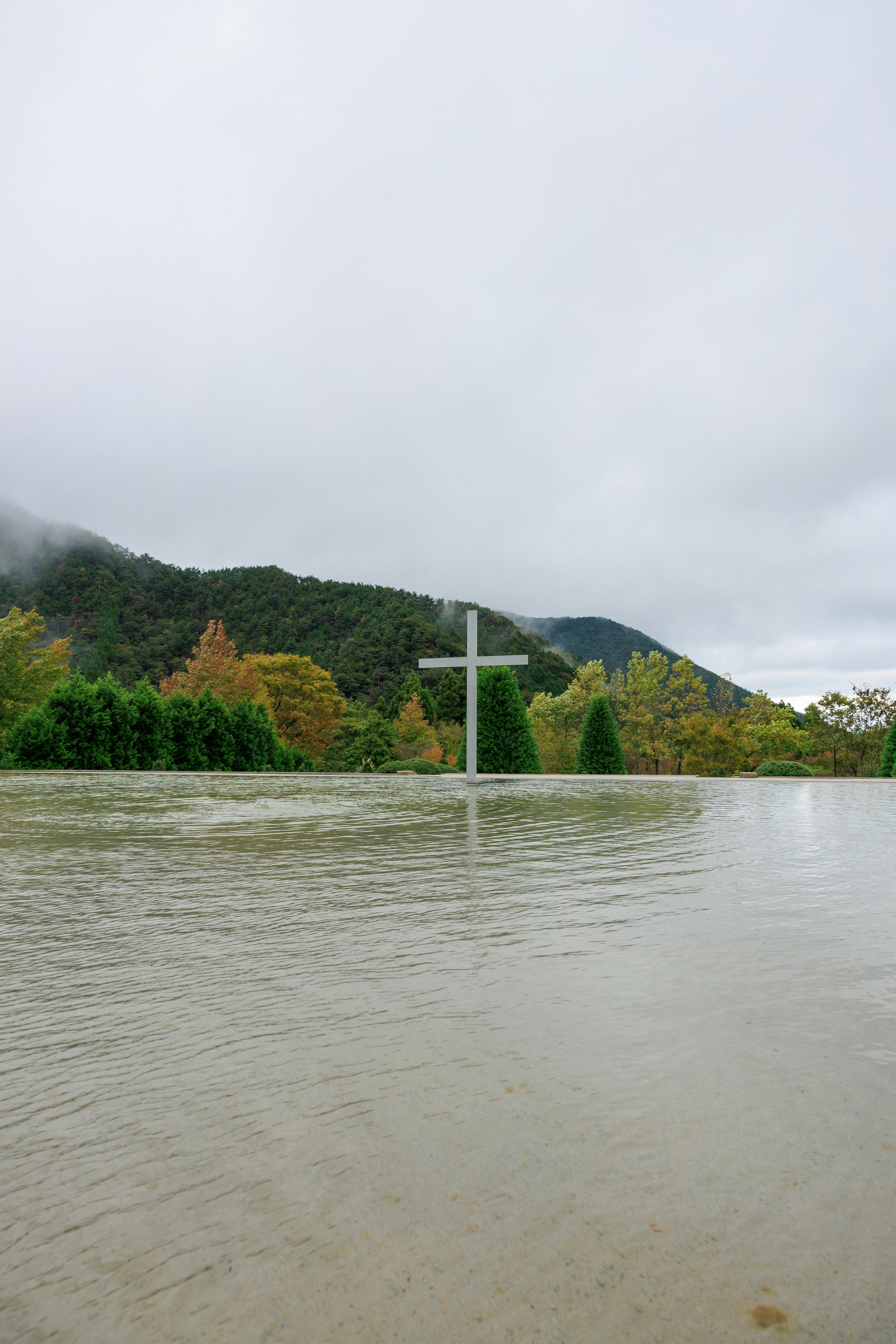 Kreuz am Seeufer mit nebligen Bergen