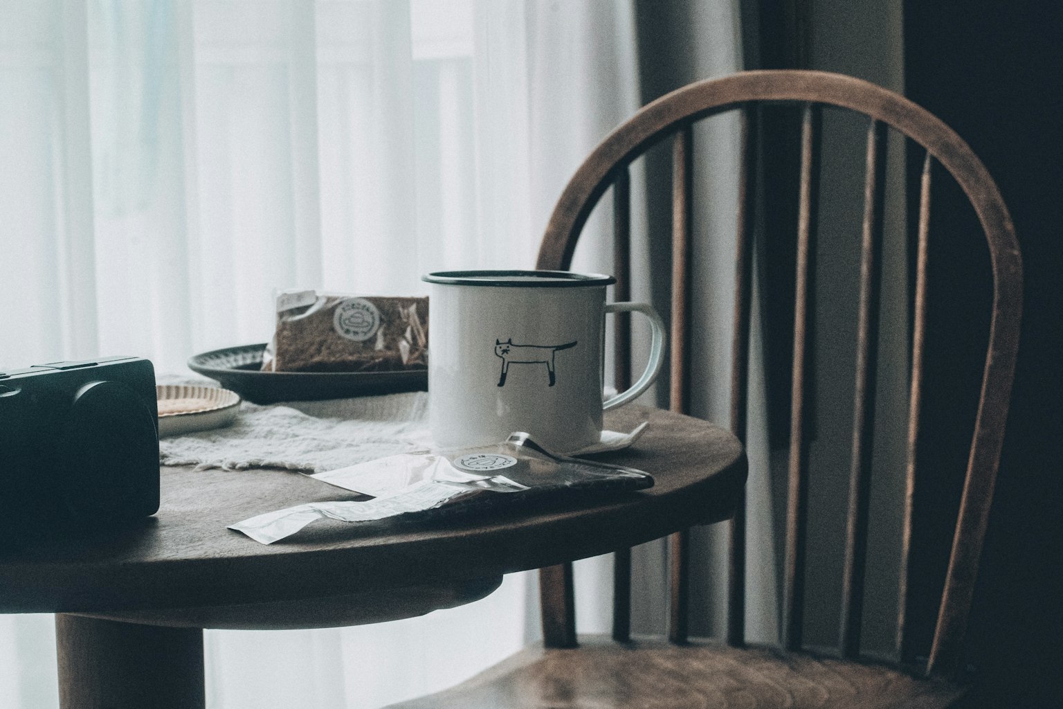 Una taza blanca sobre una mesa de madera con una caja de bocadillos y bolsitas de té