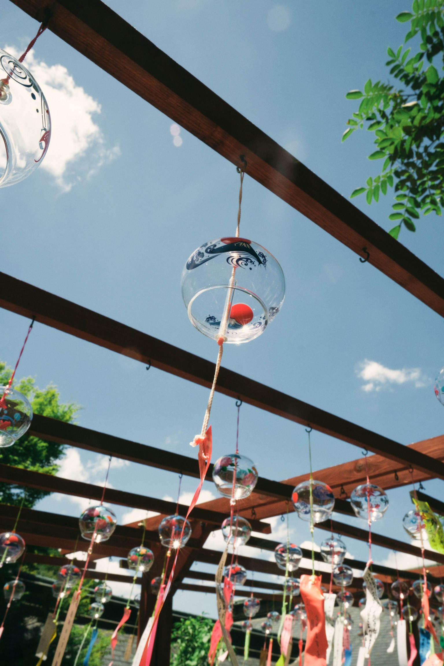 Transparente Glasobjekte hängen unter einem blauen Himmel mit bunten Bändern