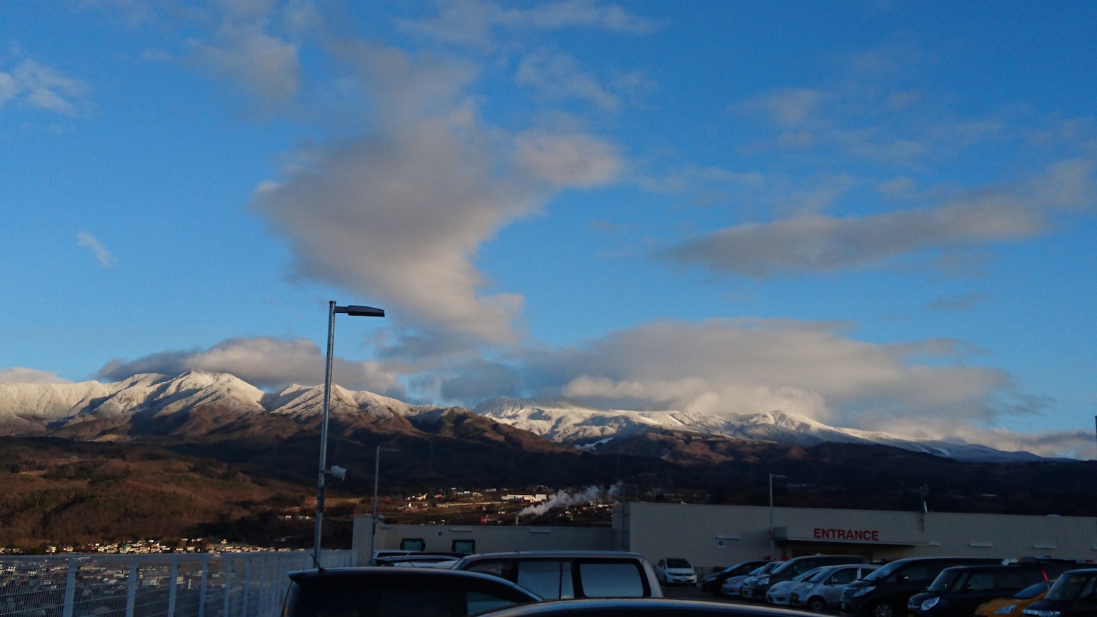 Vue panoramique de montagnes enneigées sous un ciel bleu avec des voitures garées au premier plan