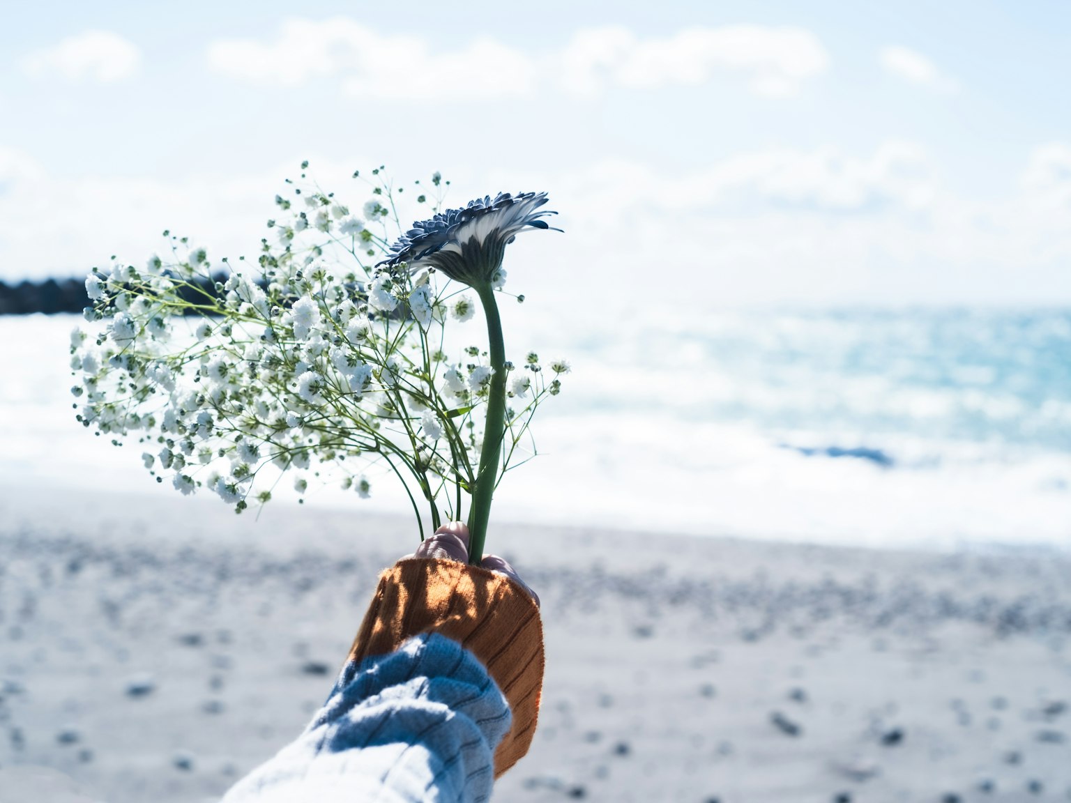 Hand, die einen Blumenstrauß am Strand hält