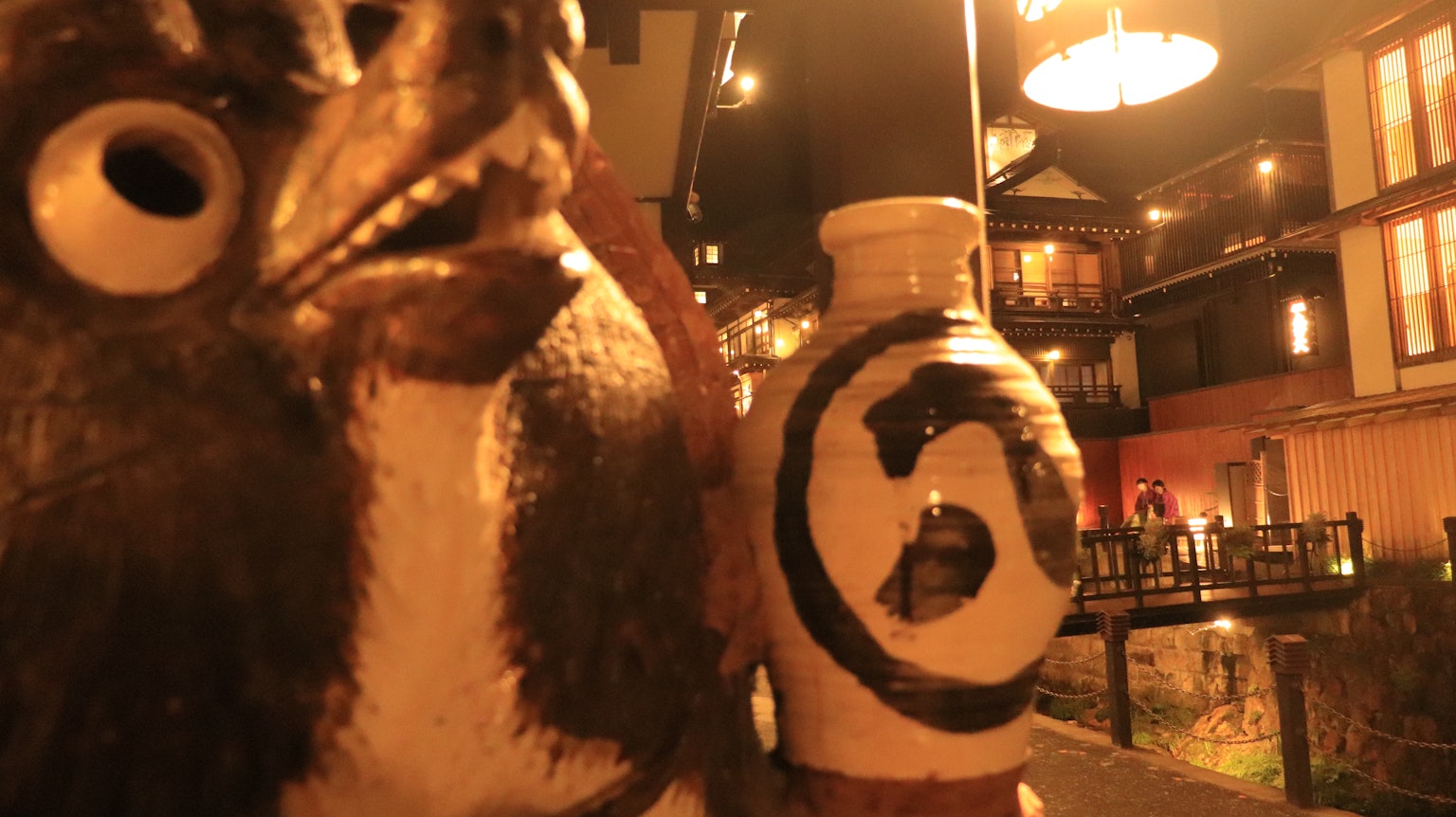 Statue en céramique de tanuki et jarre dans une rue japonaise la nuit
