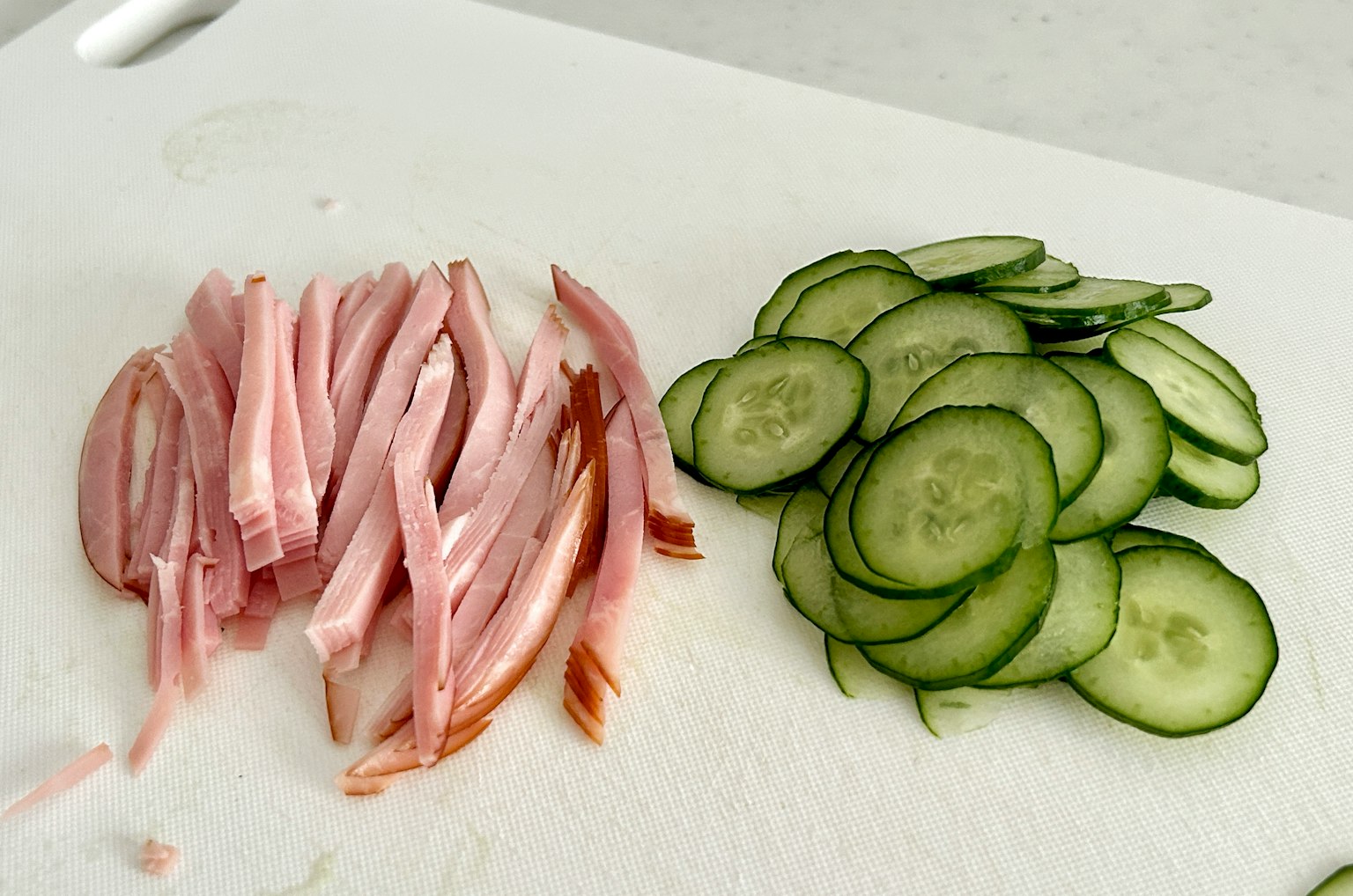 Cetrioli a fette e prosciutto rosa disposti su un tagliere bianco