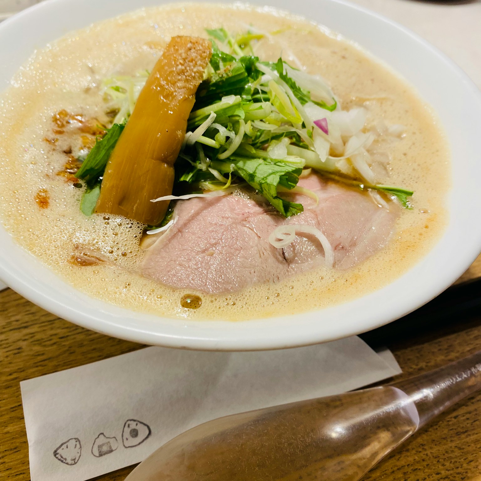 A bowl of ramen with slices of pork and assorted vegetables on top