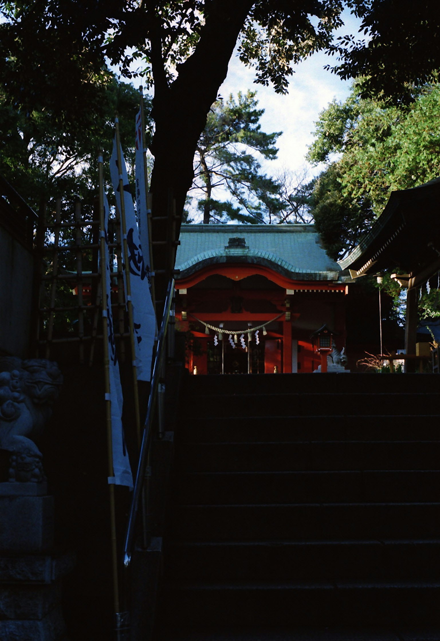 A view of a shrine with a red building seen from the top of a staircase surrounded by green trees