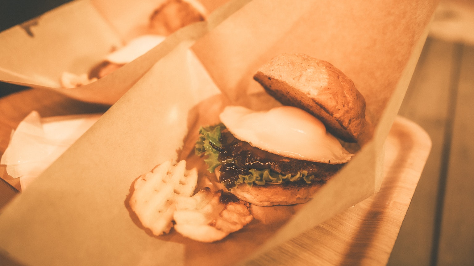 Un sándwich con lechuga y una porción de papas fritas sostenido en la mano