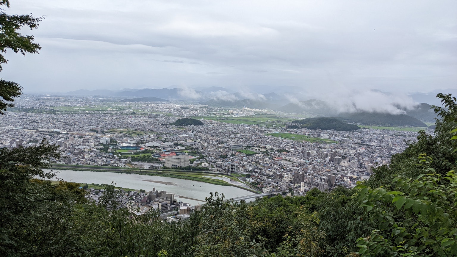 Panoramic view of a city from a mountain top with cloudy sky and lush greenery