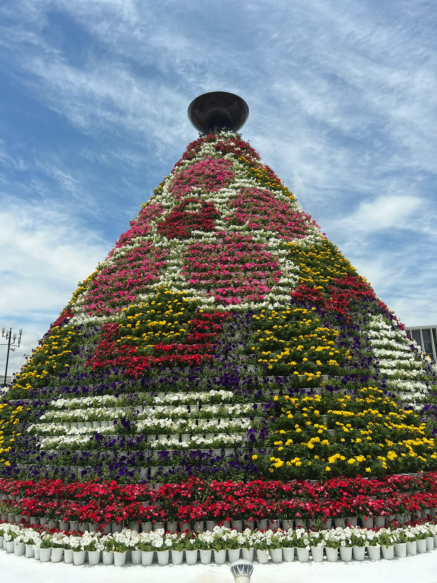 Pyramid-shaped floral arrangement with colorful flowers and a pot on top under a blue sky