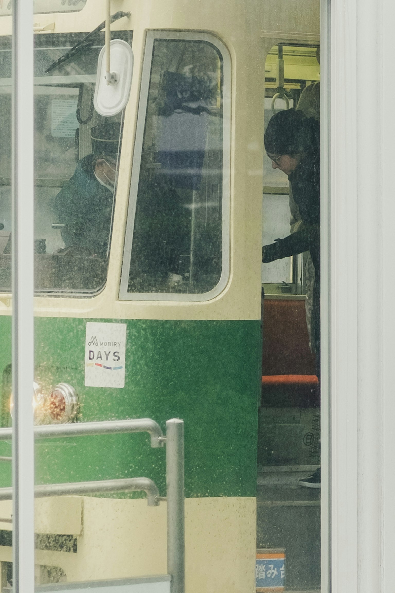 Vista attraverso la finestra della cabina del conducente di un tram verde e crema con un passeggero