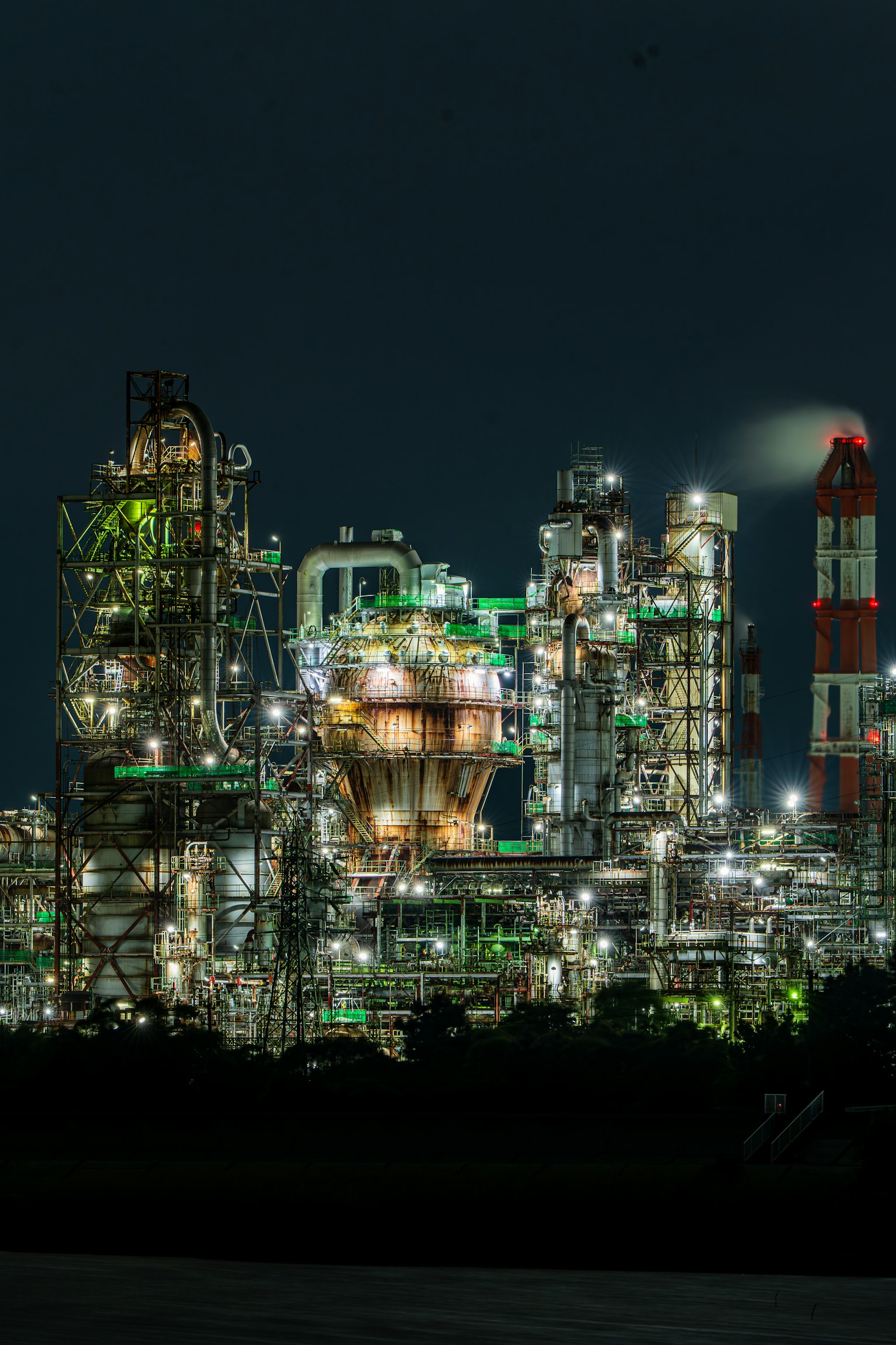 Paysage industriel nocturne avec des tours et des cheminées lumineuses lumières vertes et orange vives