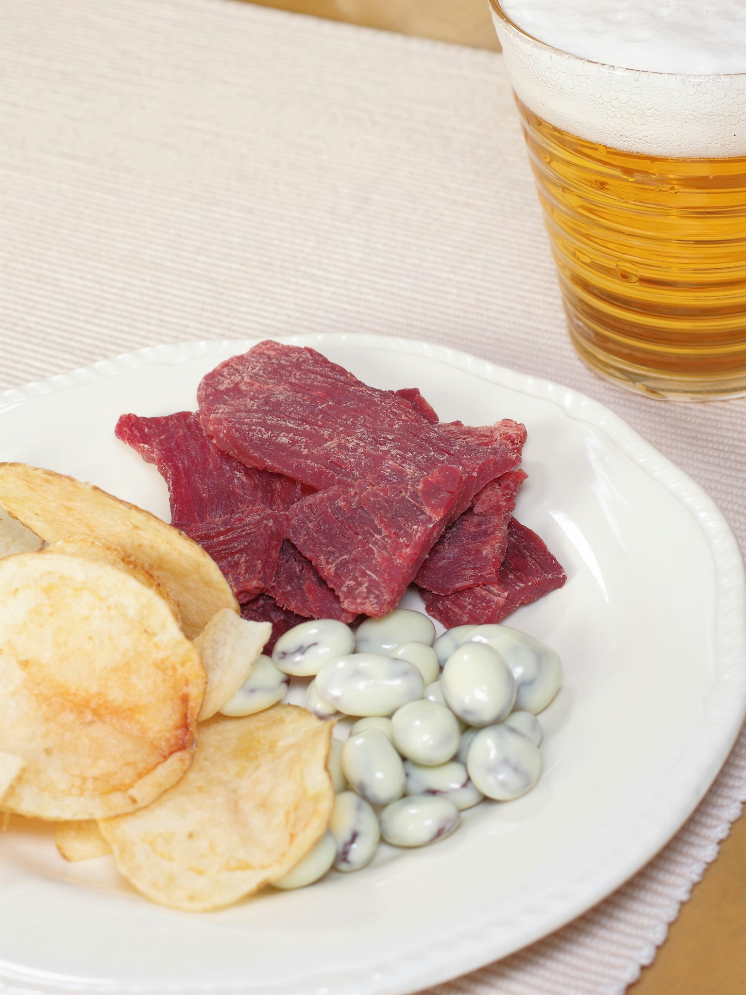 Assiette de collations avec du jerky des chips de pommes de terre et des haricots blancs accompagnée d'un verre de bière