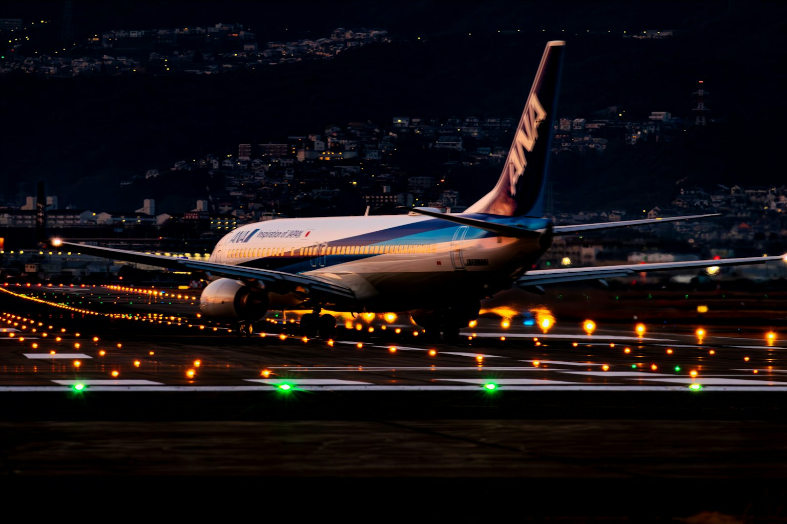 夜間在跑道上滑行的飛機，背景是城市燈光