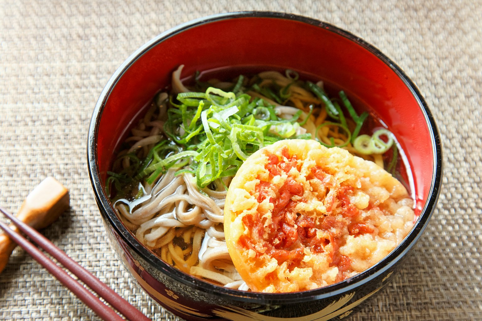 บะหมี่โซบะในชามสีแดงพร้อมเทมปุระและต้นหอม
