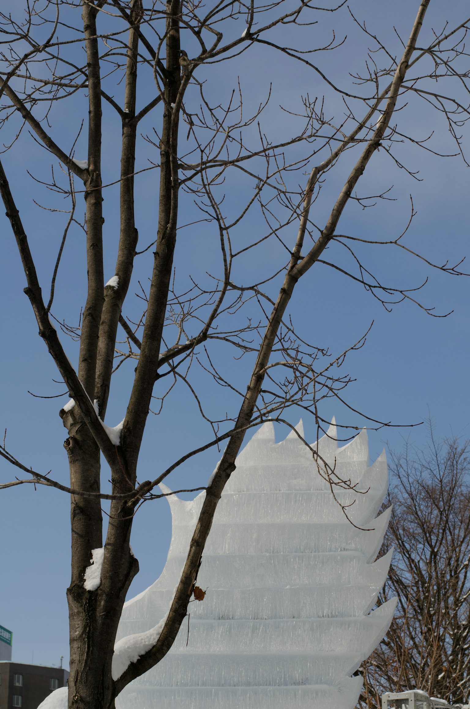 Un albero con rami spogli accanto a una scultura di neve sotto un cielo invernale