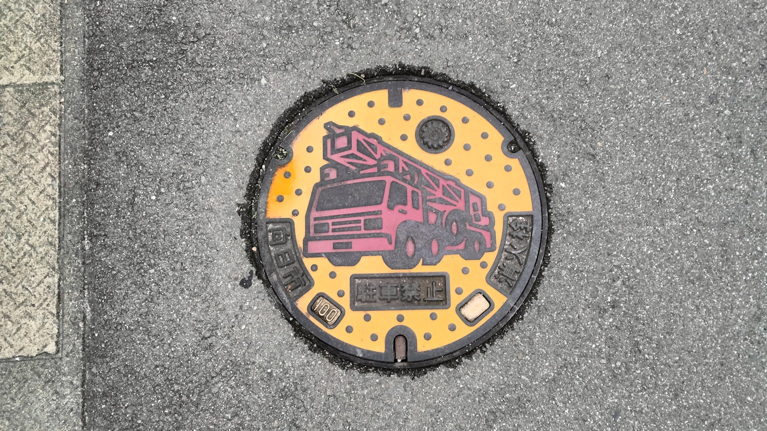 Una tapa de alcantarilla con una ilustración de un camión de bomberos rosa sobre un fondo amarillo