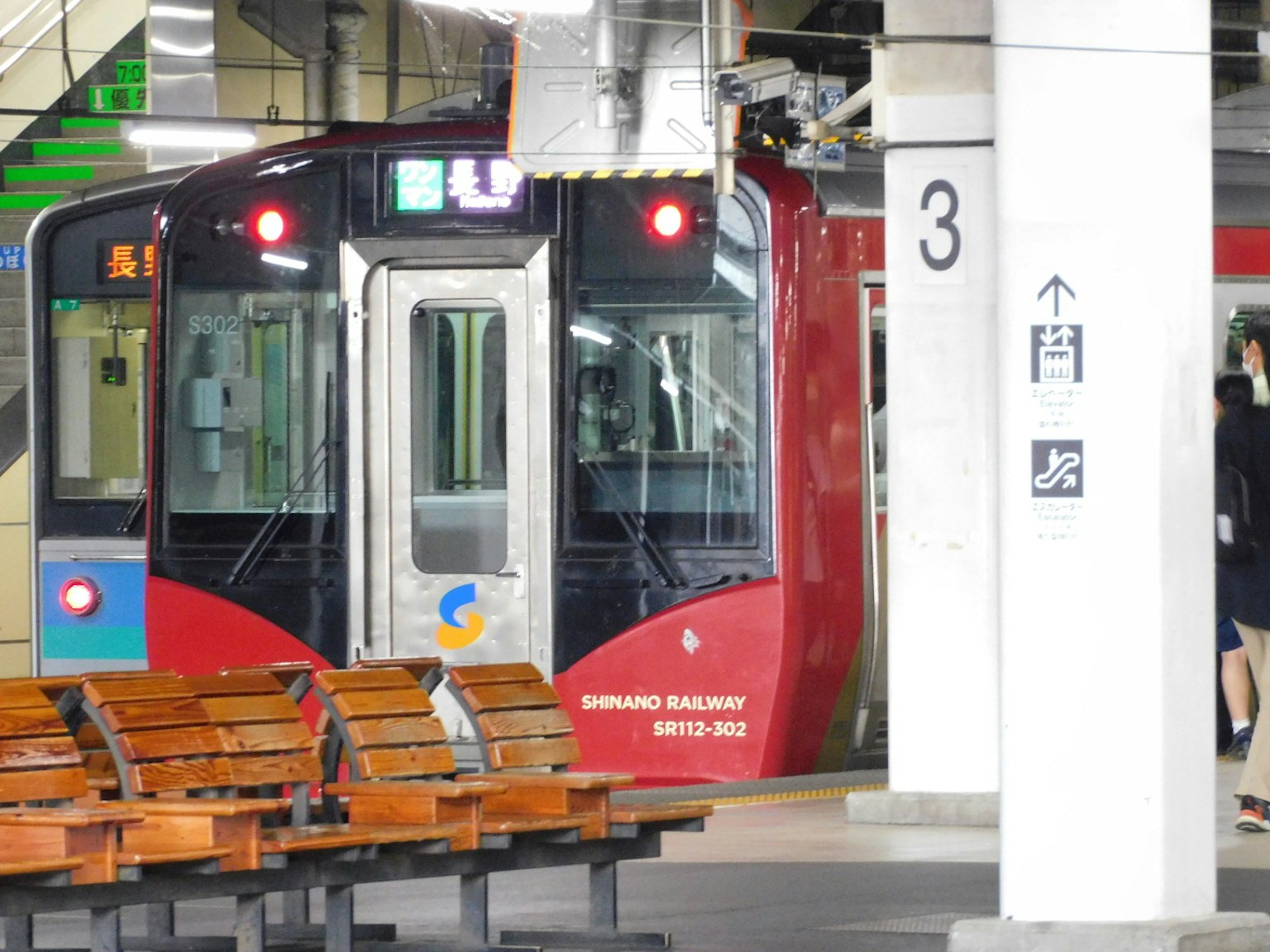 รถไฟสีแดงที่สถานีมีม้านั่งและเสาเห็นได้