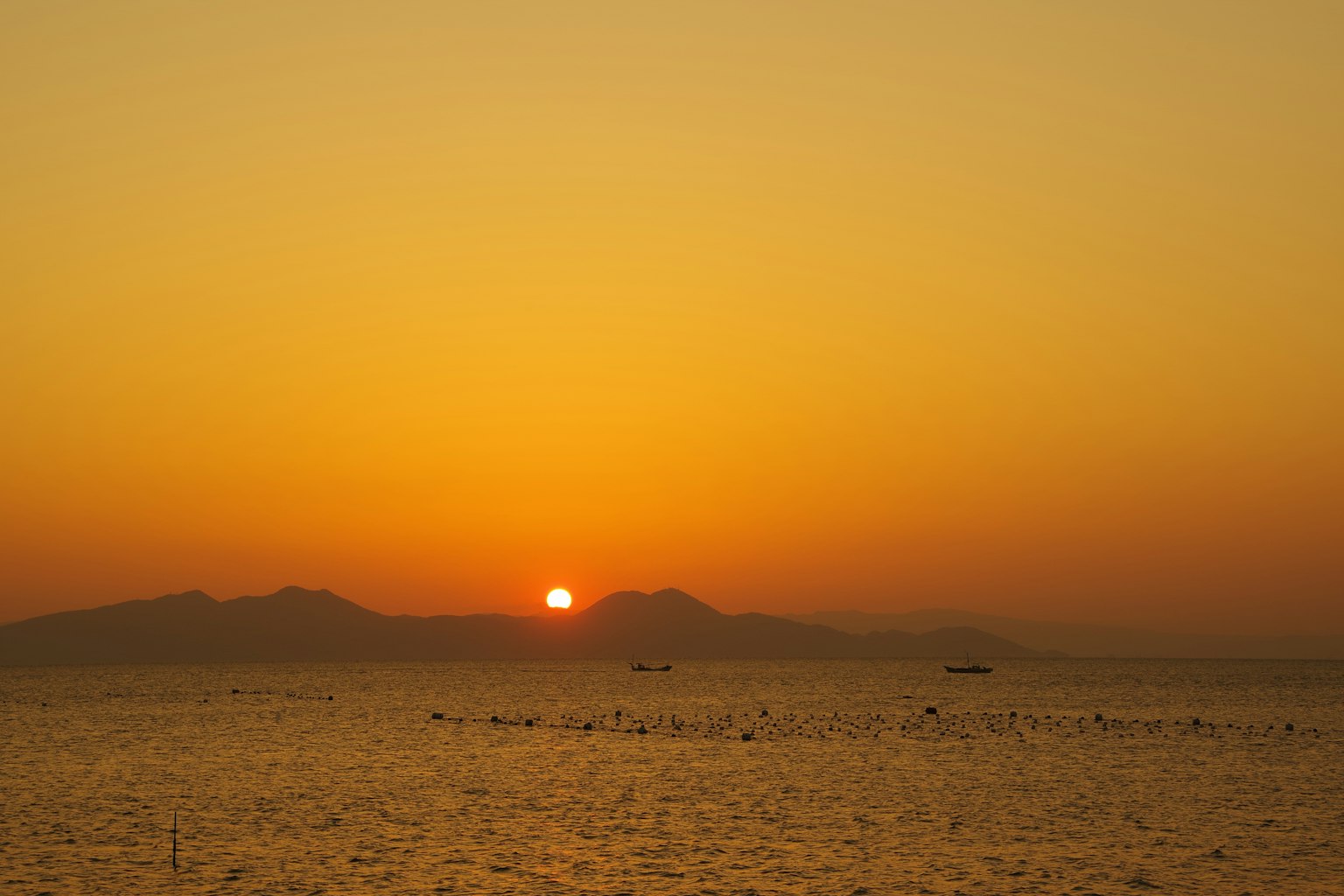 夕阳在橙色天空中落入海洋，山的轮廓