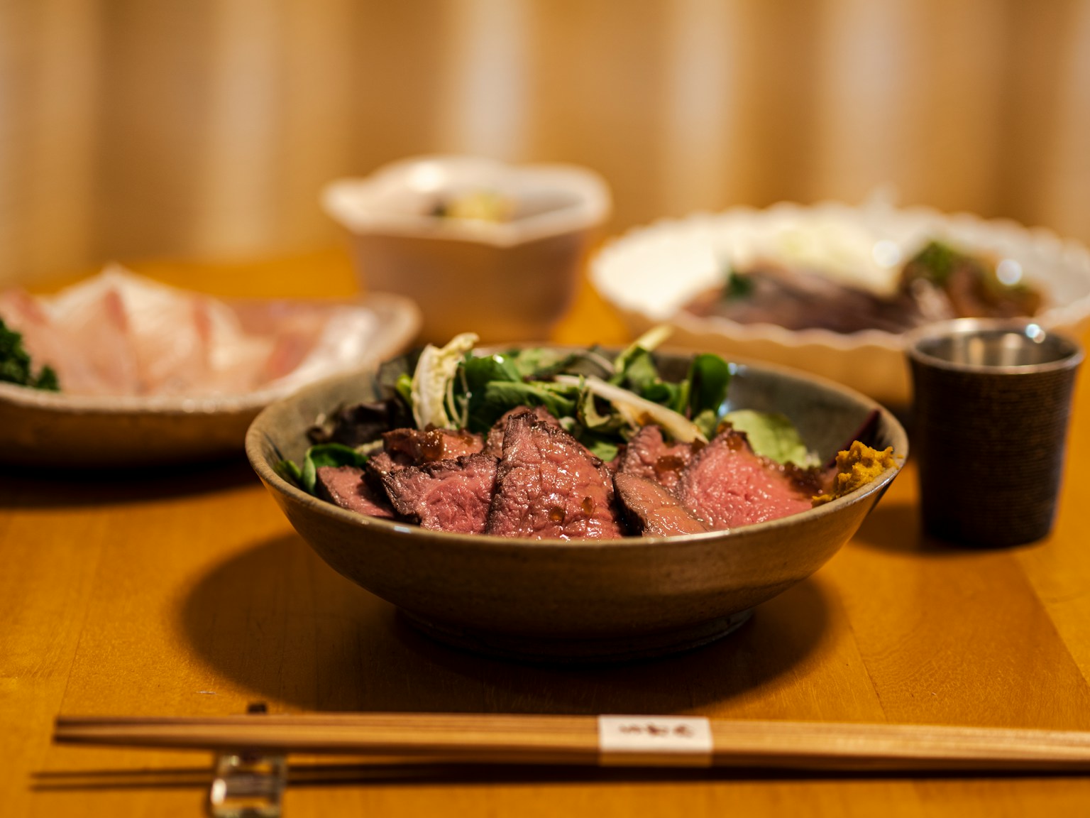 美味的日本餐呈現，中間是牛肉碗，周圍有生魚片和配菜，放在木桌上