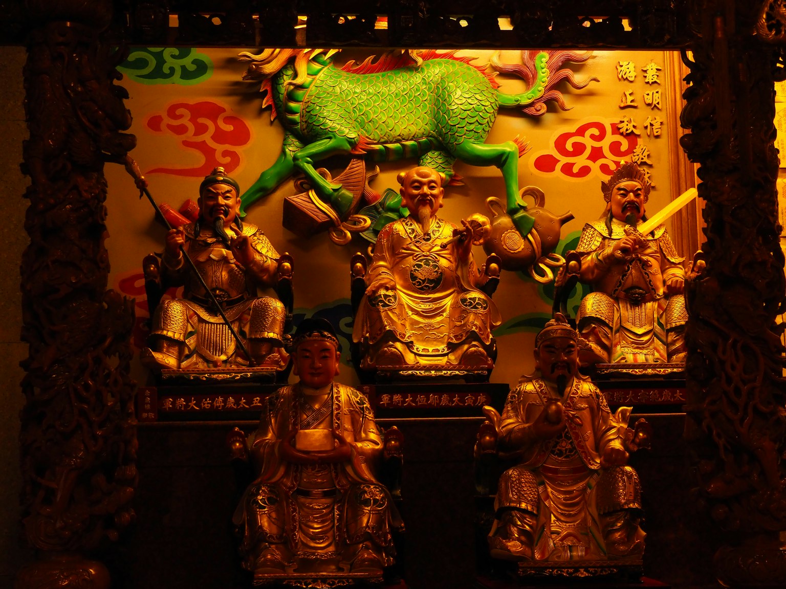 Estatuas doradas de deidades dispuestas con una figura de caballo verde al fondo