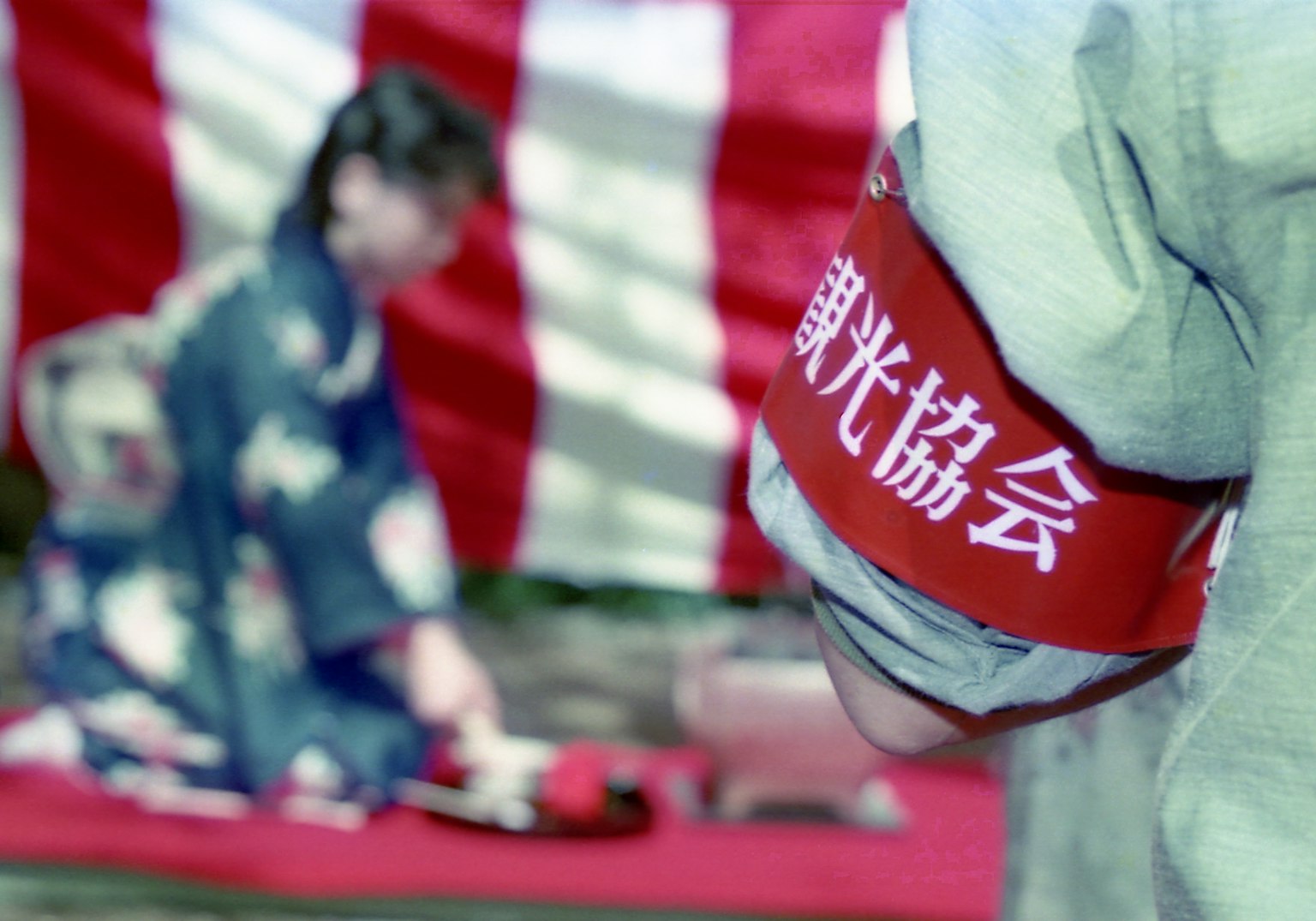 穿着和服的人，佩戴红色带子上有文字，背景是条纹