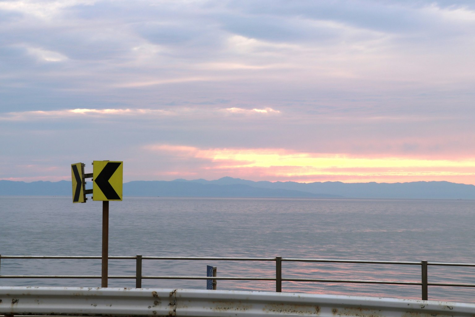 Curved road sign with coastline and sunset in the background