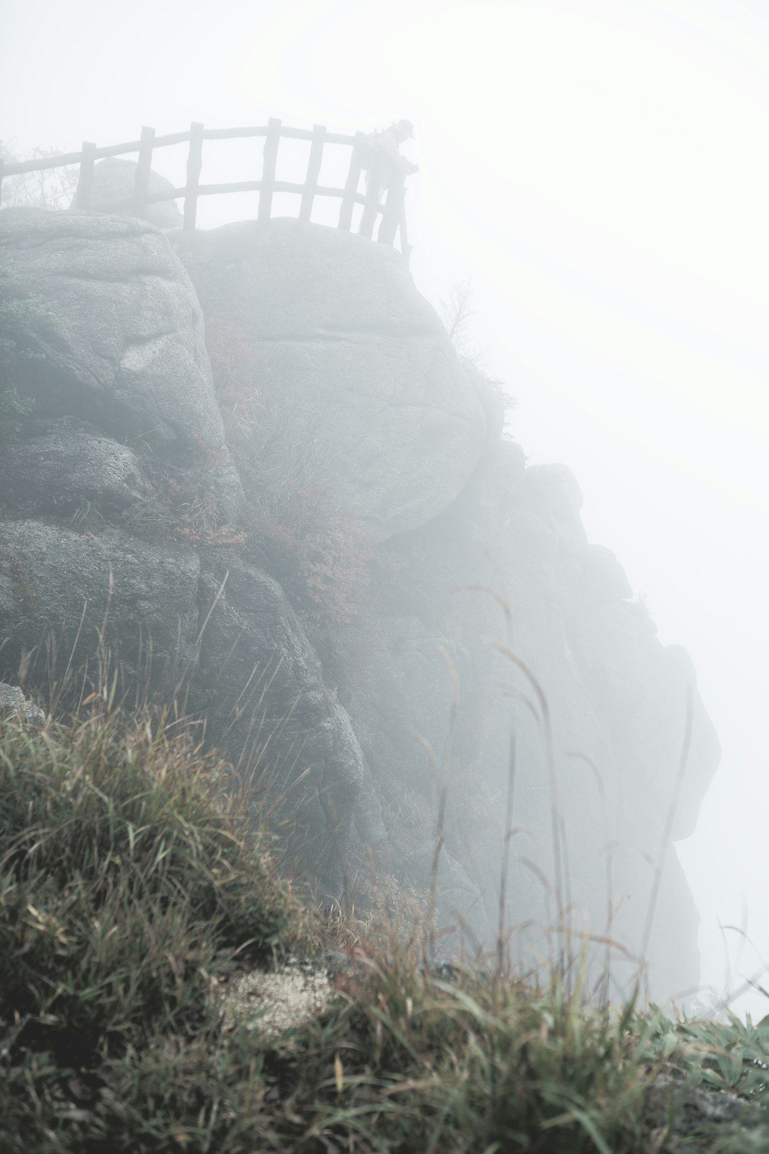 霧に包まれた岩の崖と木製の手すりが見える風景