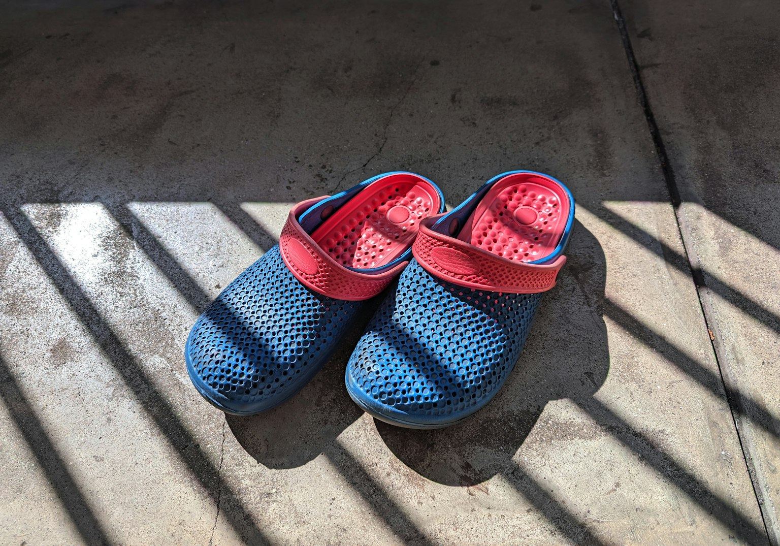 Sabots en mesh bleu et rouge posés sur un sol en béton avec des ombres
