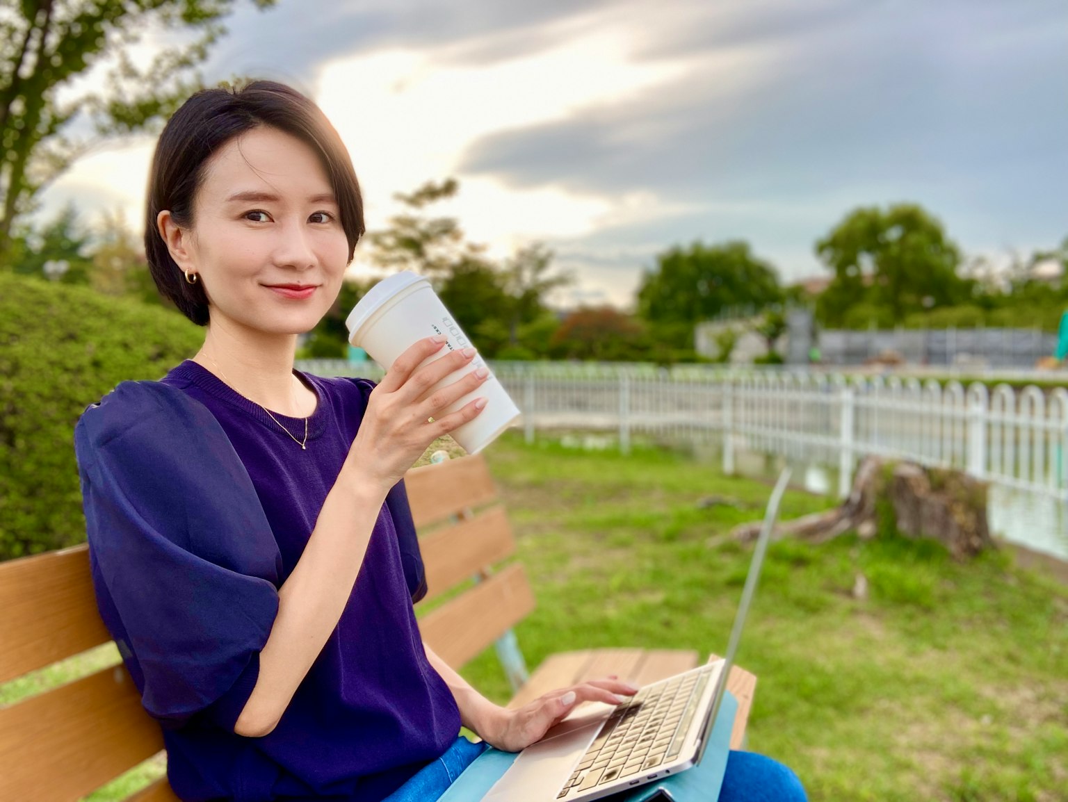 公园长椅上坐着的女性，一边喝咖啡，一边用笔记本电脑工作
