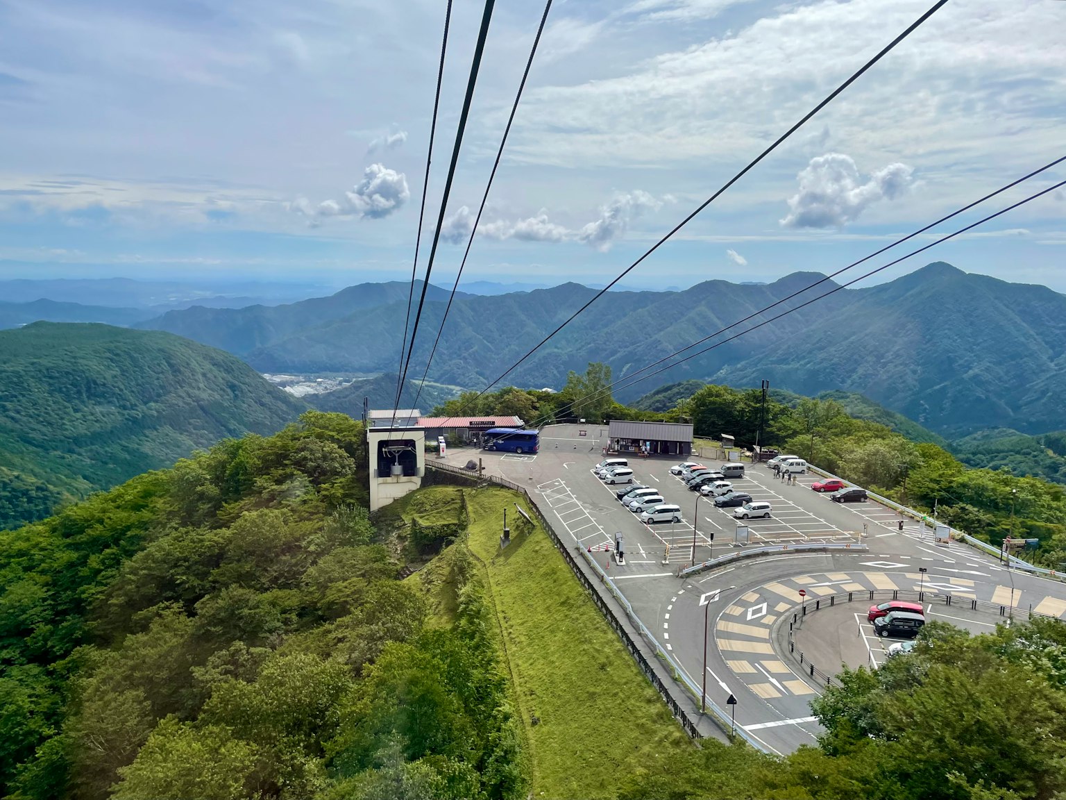 View from the top of a mountain featuring a cable car station and parking area