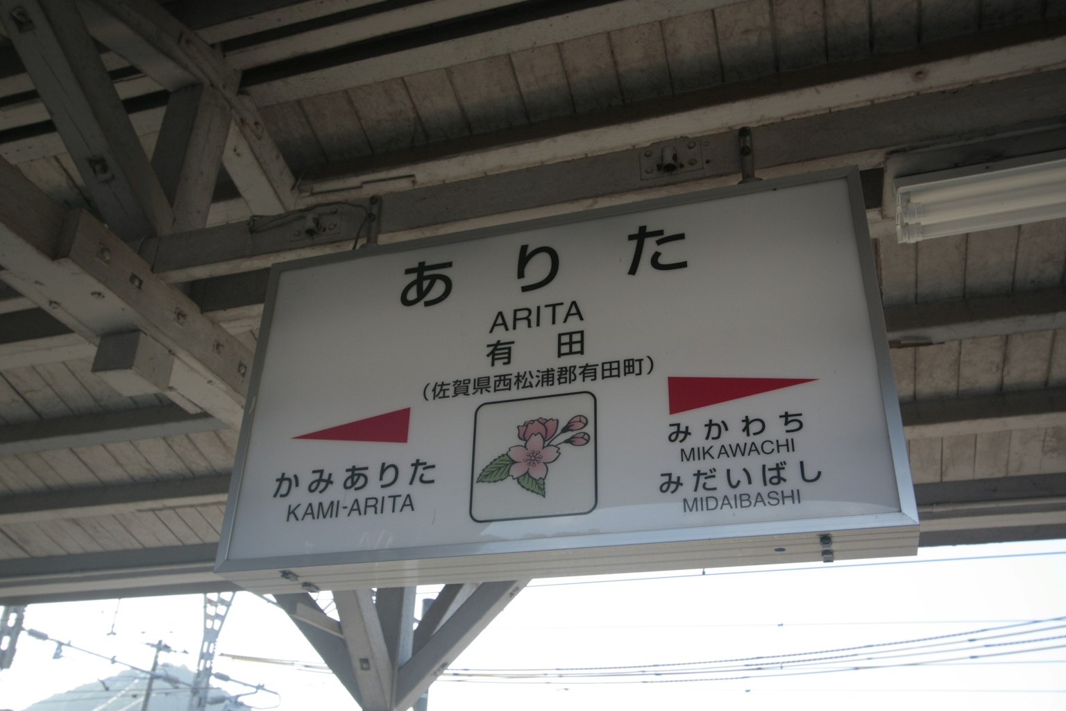 Papan stasiun Arita dengan panah arah dan karakter Jepang