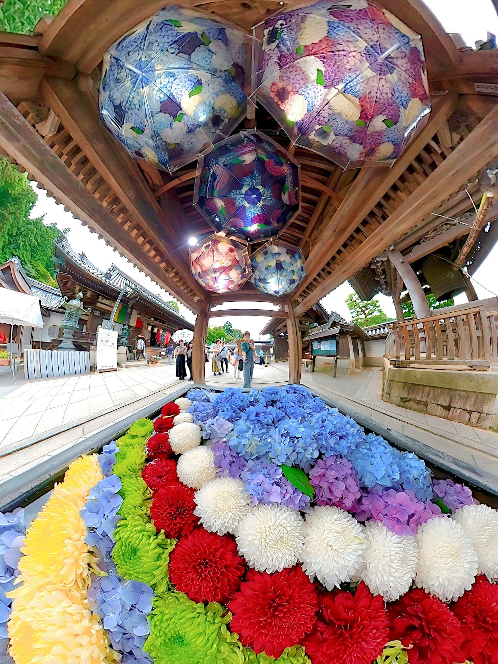 bunte Blumenarrangements entlang eines Tempelweges mit hängenden Windspielen